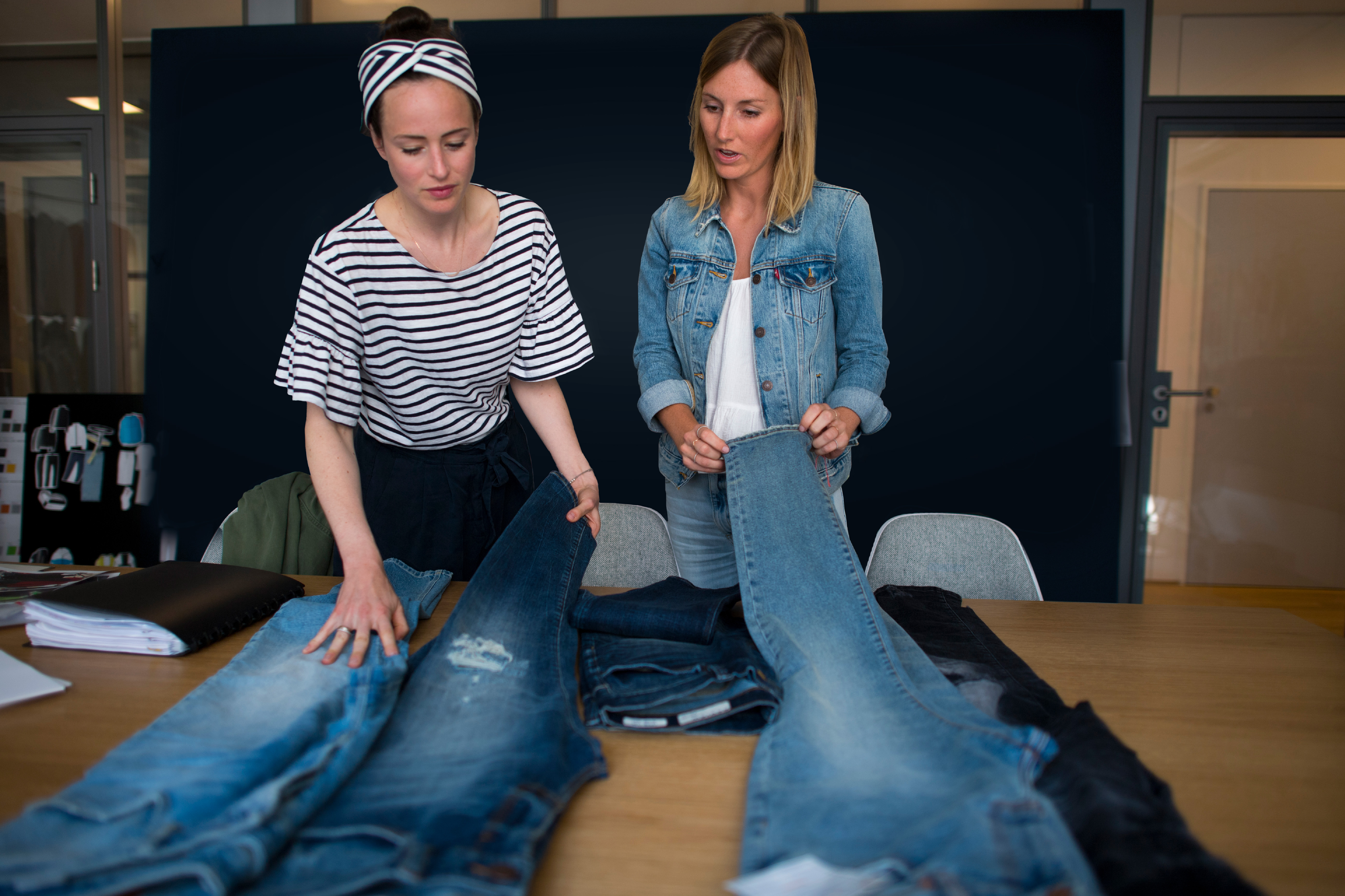 Zwei Frauen analysieren Jeanshosen, die auf dem Tisch vor ihnen liegen.