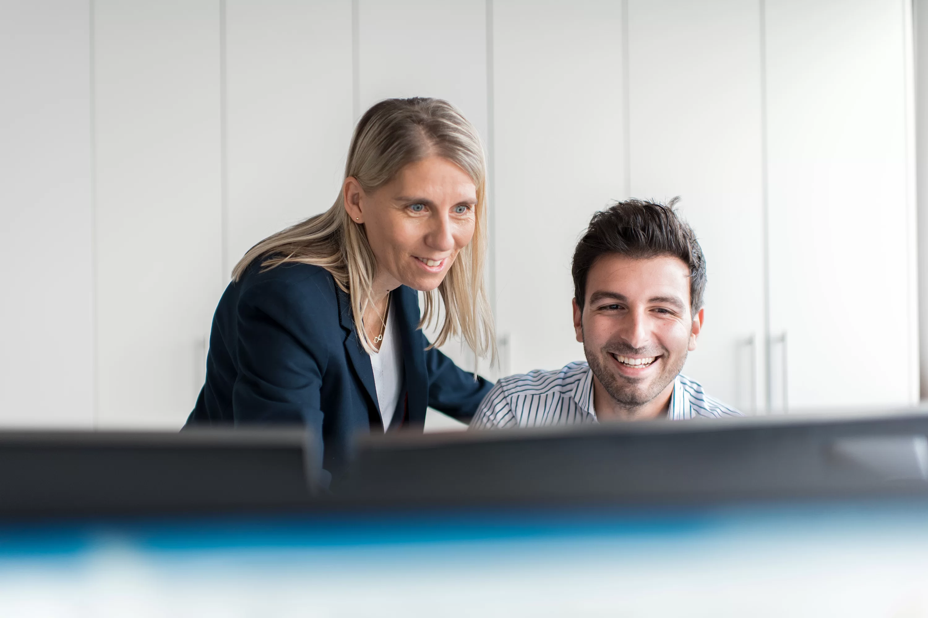Eine Frau und ein Mann arbeiten gemeinsam am Computer und lächeln.