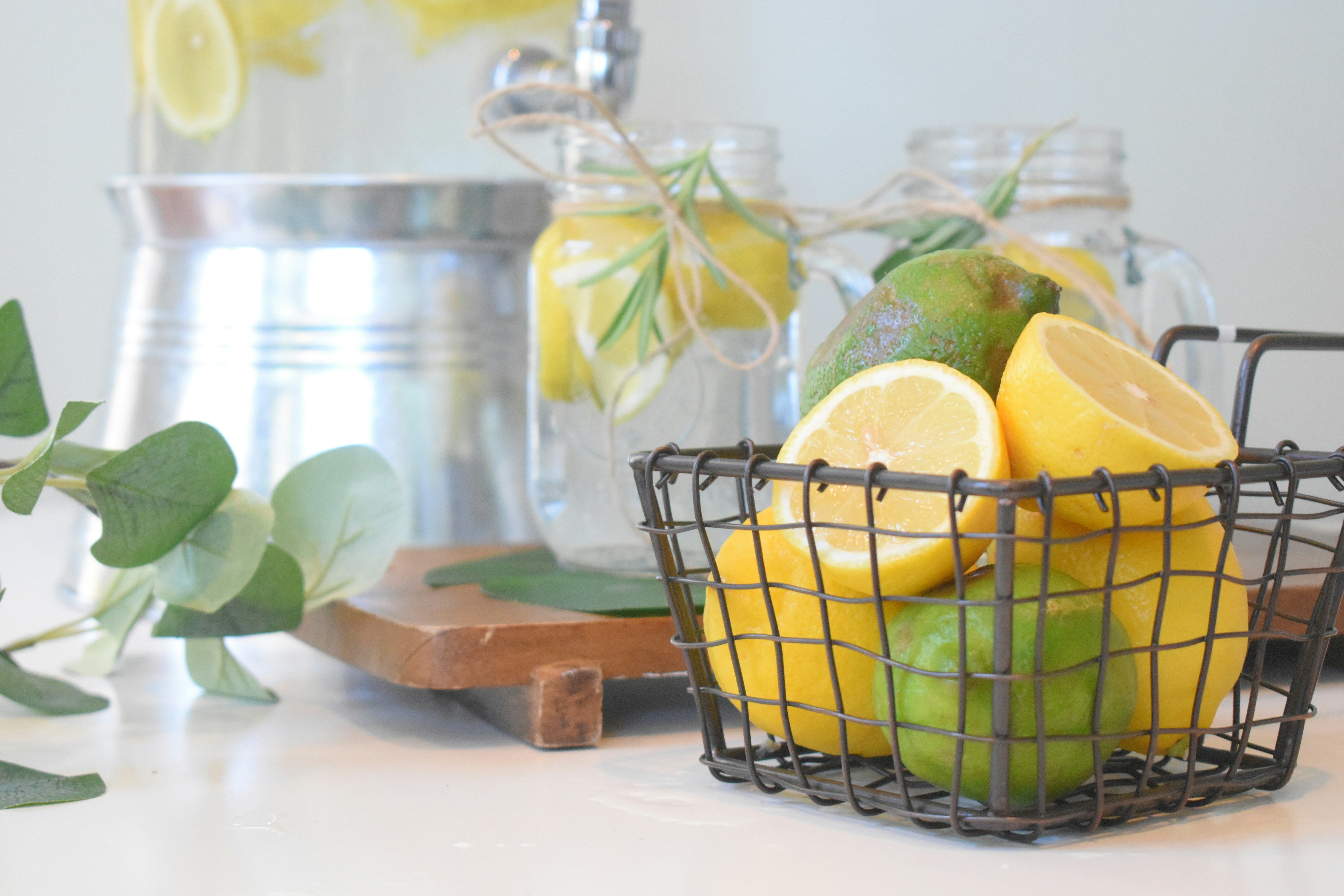 Ein Korb mit Zitronen, im Hintergrund Trinkgläser mit Wasser und Zitronenscheiben