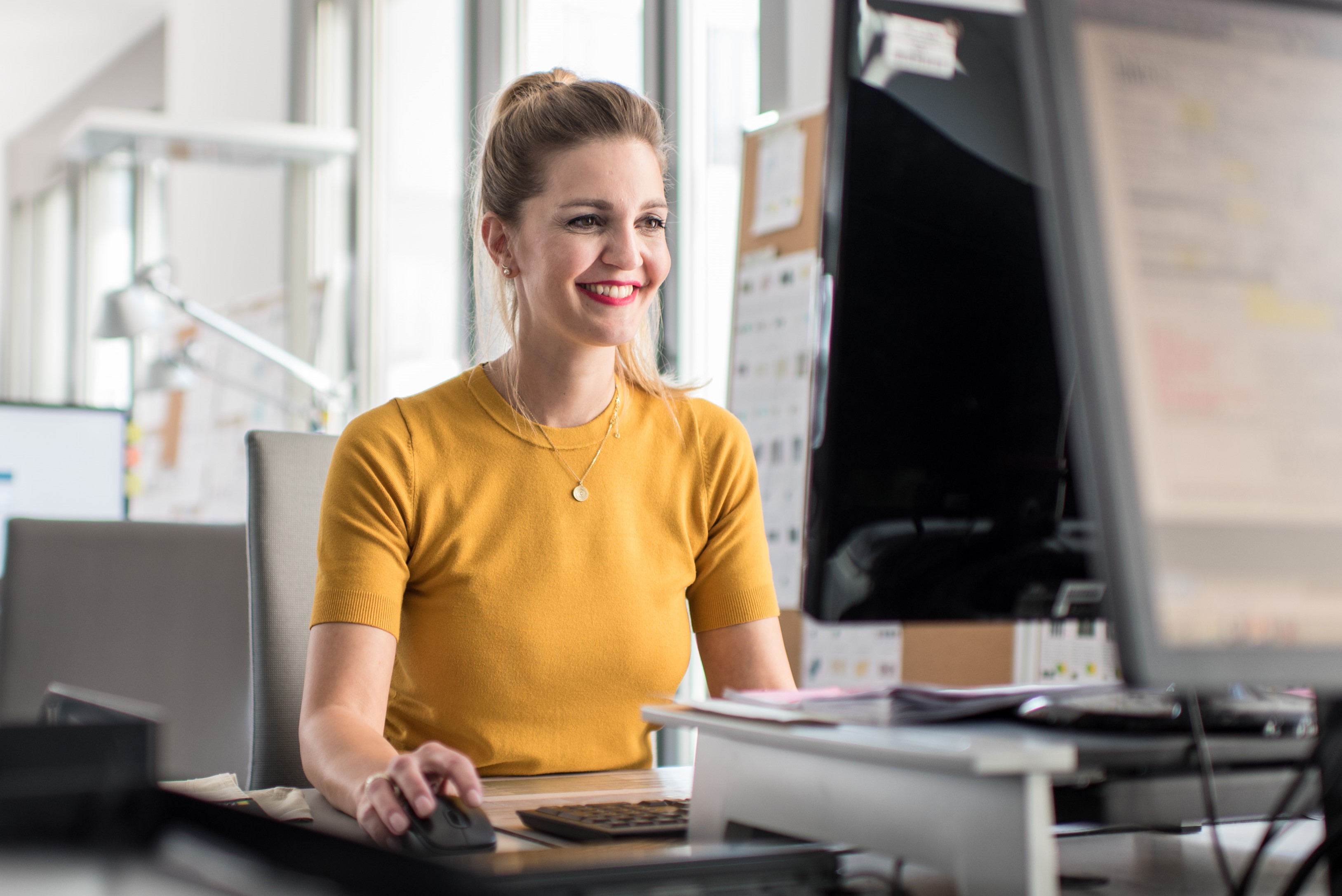 Eine junge Frau sitzt am Schreibtisch und arbeitet am Computer.