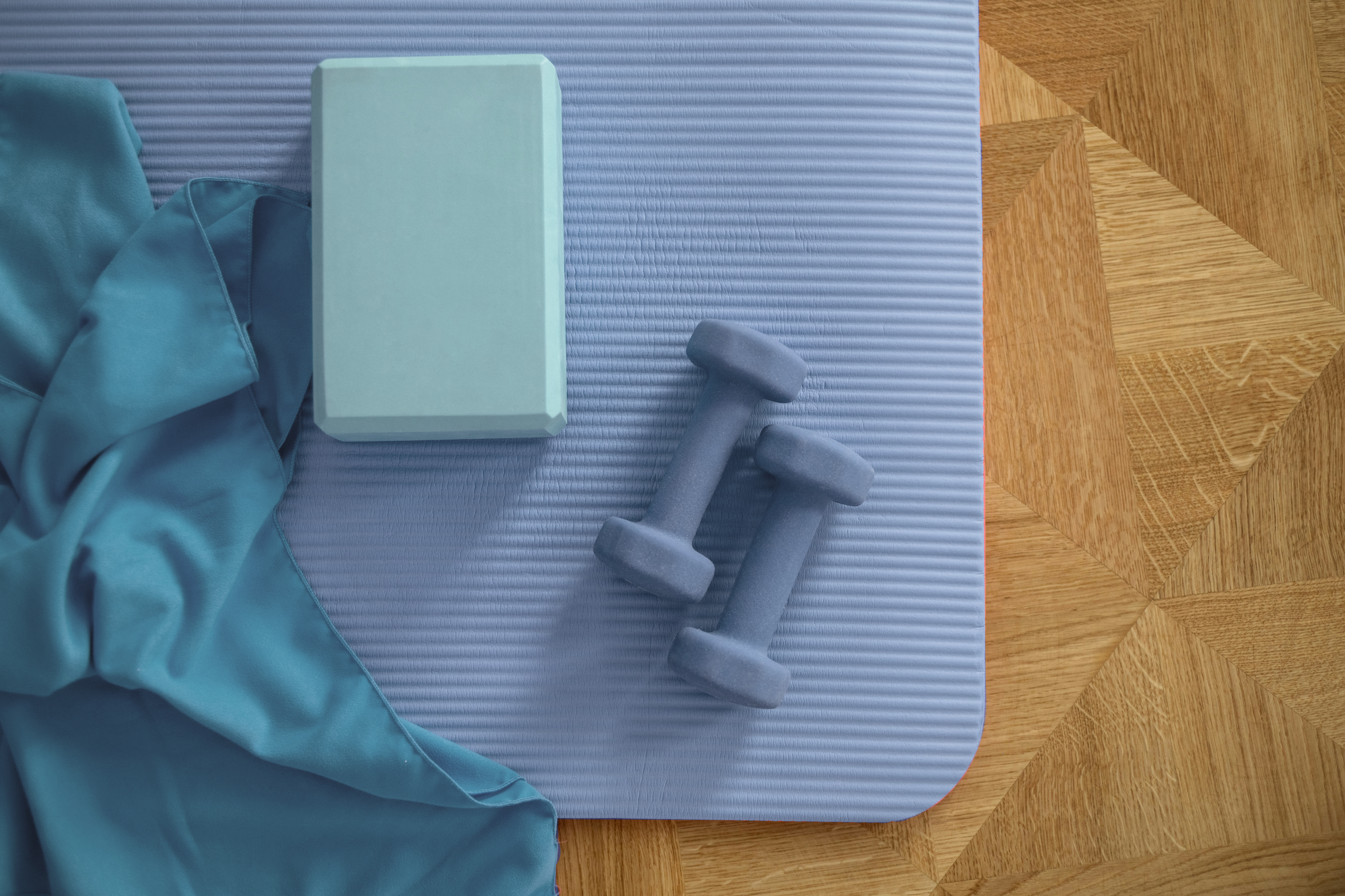 Ein Handtuch, eine Yogaklotz und Hanteln liegen auf einer Fitnessmatte auf einem Holzboden.