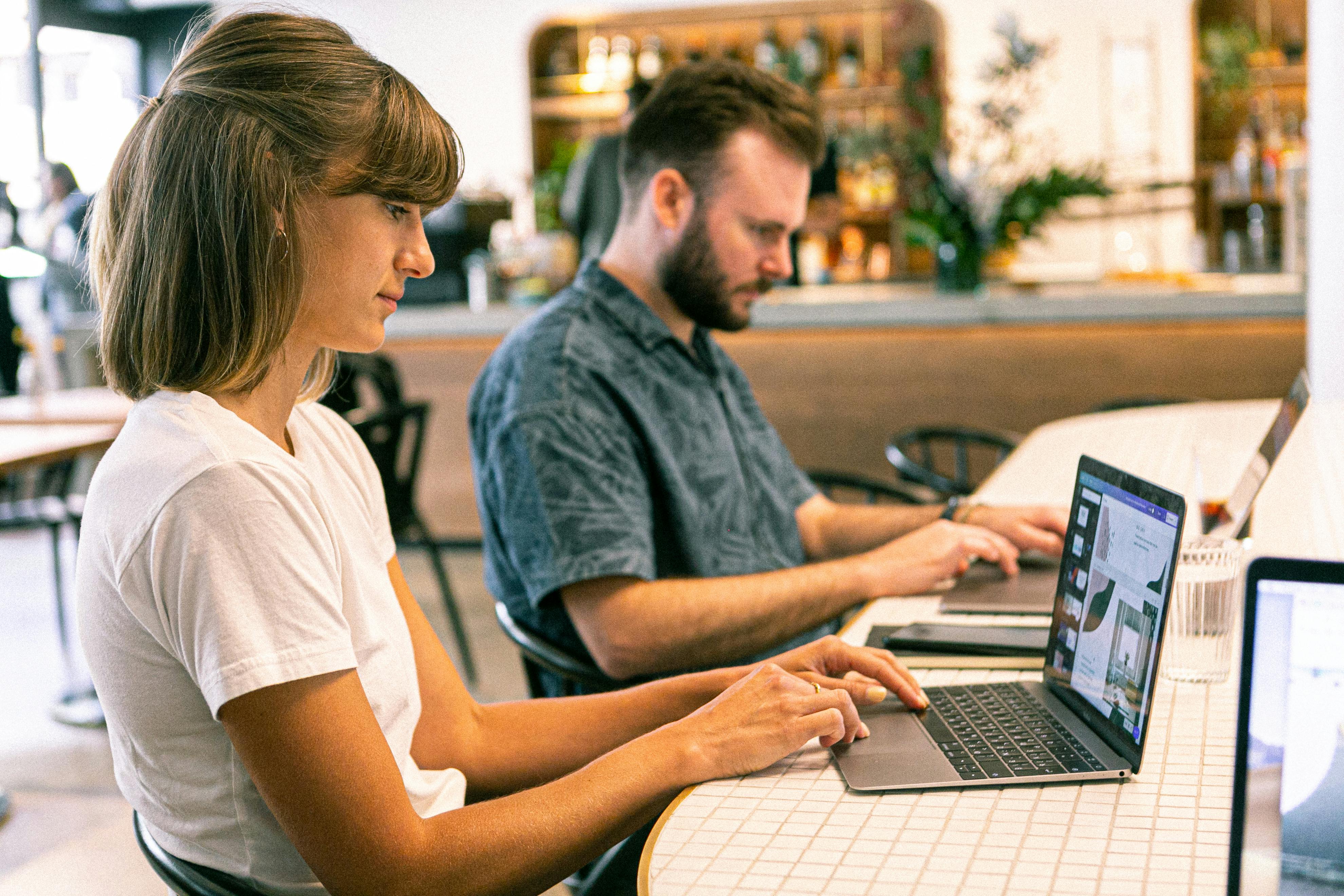 Eine Frau und ein Mann sitzen an einem Tisch und arbeiten an ihren Laptops.